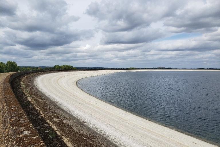Curved reservoir shoreline with white gravel edge and calm water under a cloudy sky